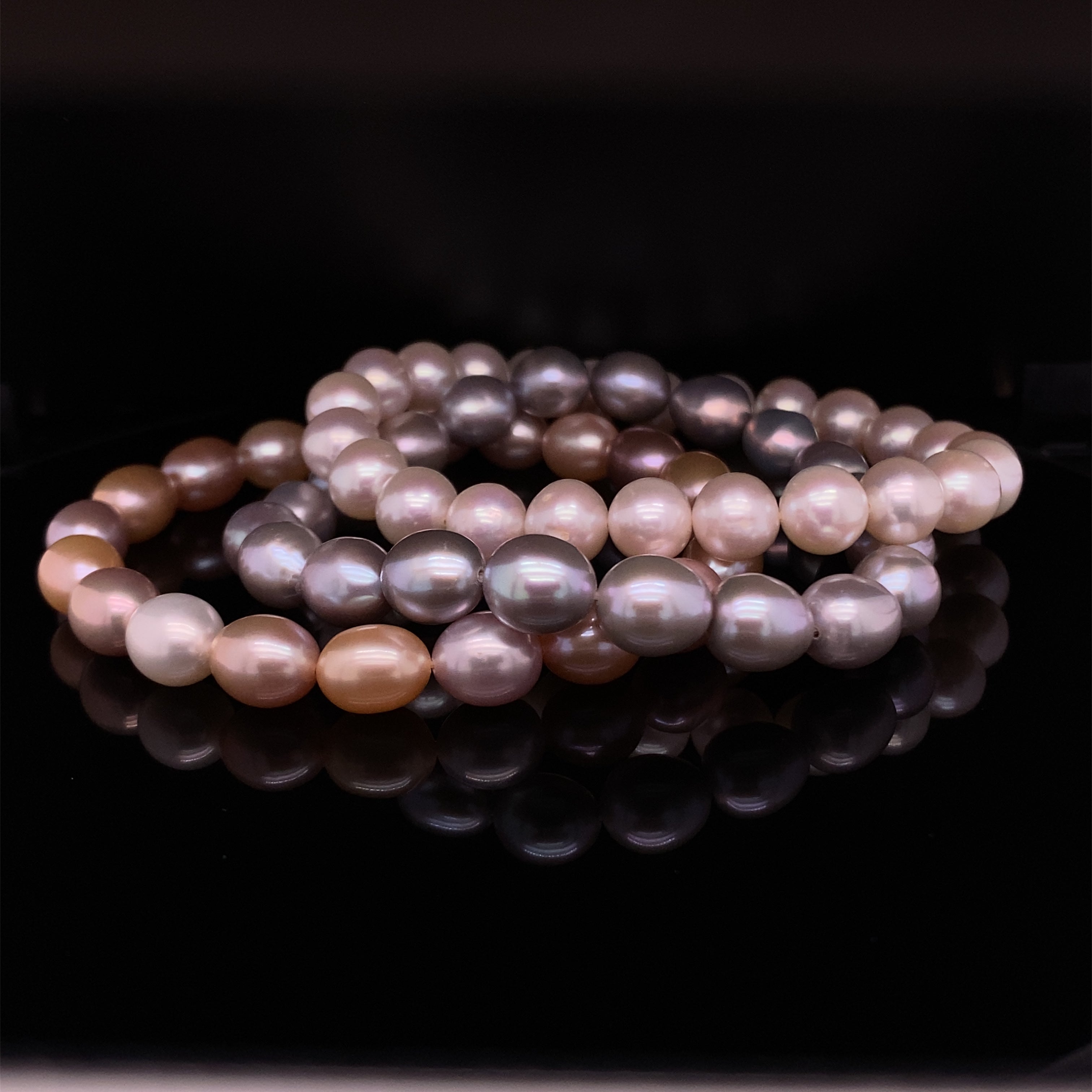 armbanden van zoetwaterparels in wit, roze en grijs op een zwarte achtergrond